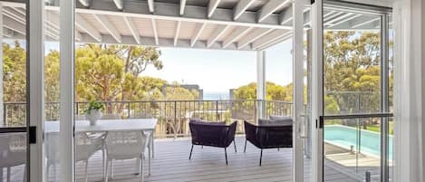 Un espace extérieur abrité, avec une table et des chaises, une piscine en arrière-plan et une vue sur les arbres.
