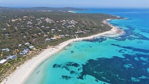 An aerial view of a coastal area with a beach, houses, and clear blue waters.