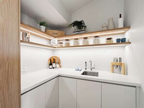 Una cocina moderna con armarios blancos, un lavamanos integrado y estantes de madera sobre la encimera.