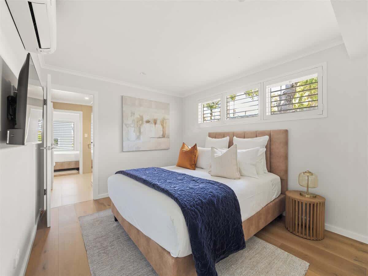 A bedroom with a bed, a bedside table, a TV, and a window with blinds.