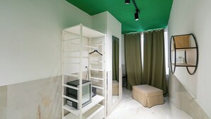 A room with a green ceiling, white walls, a white shelving unit, a beige ottoman, and a black storage unit. - GREROS TOLEDO H. by Clapa Group dislocated hospitality (Naples)