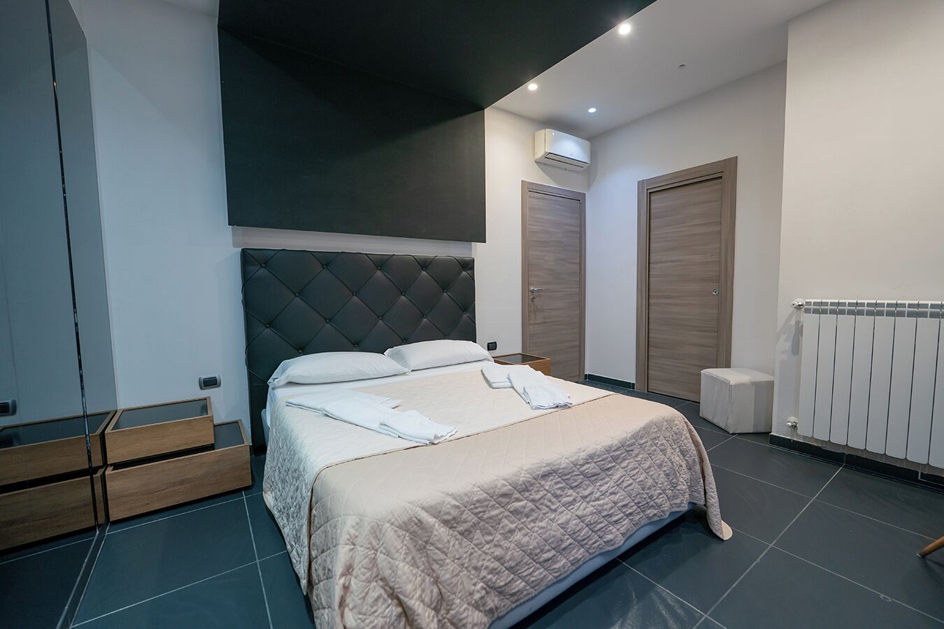 Una camera da letto moderna con un letto grande, una testiera scura, un comodino, un armadio e un termosifone.
