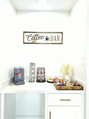 A coffee bar setup with a coffee machine, a mug holder, and a basket of snacks.