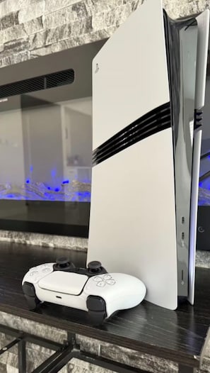 A gaming console and controller on a dark wooden surface with a stone wall in the background.