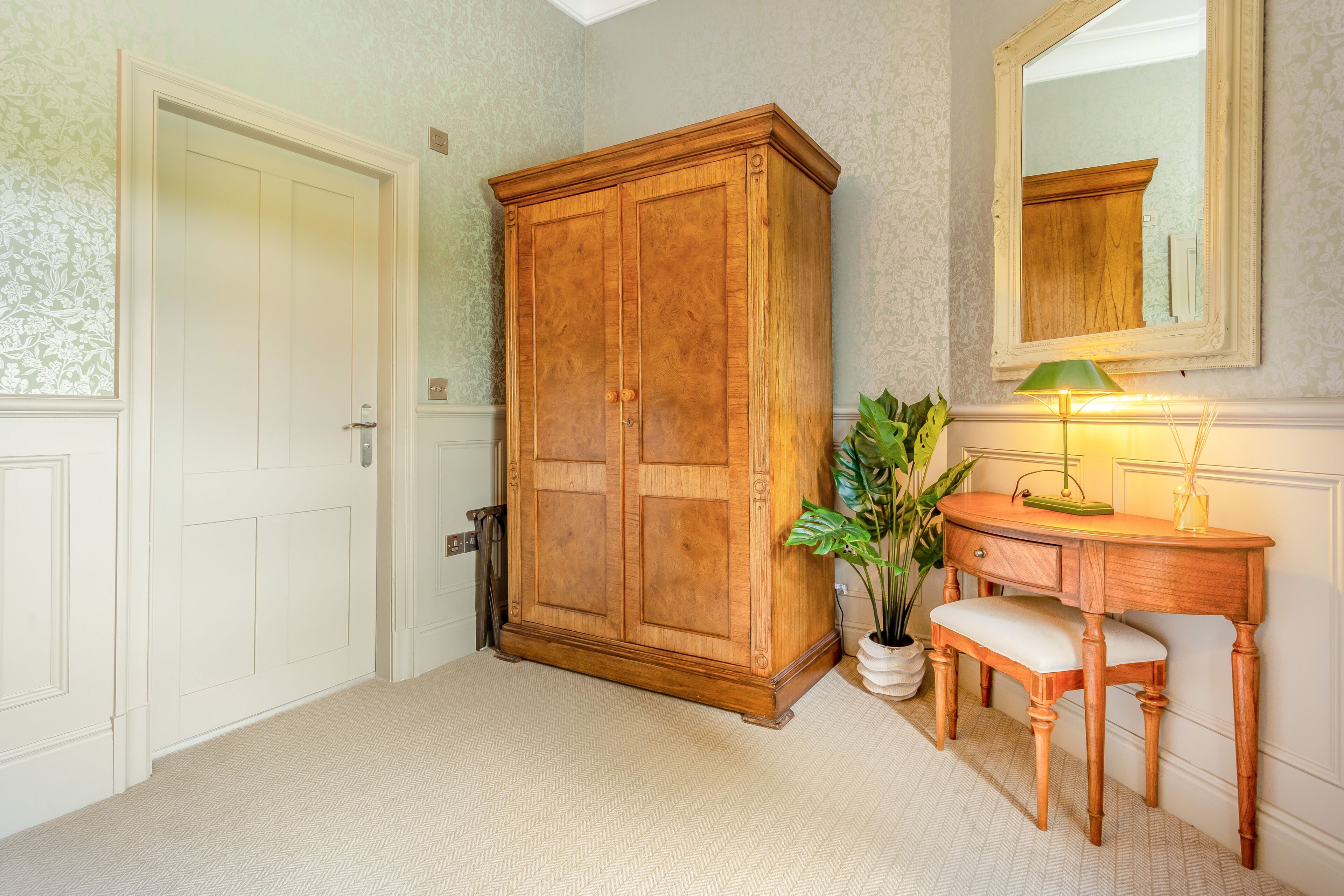 Une pièce comprenant une grande armoire en bois, un bureau avec une lampe et un miroir accroché au mur.