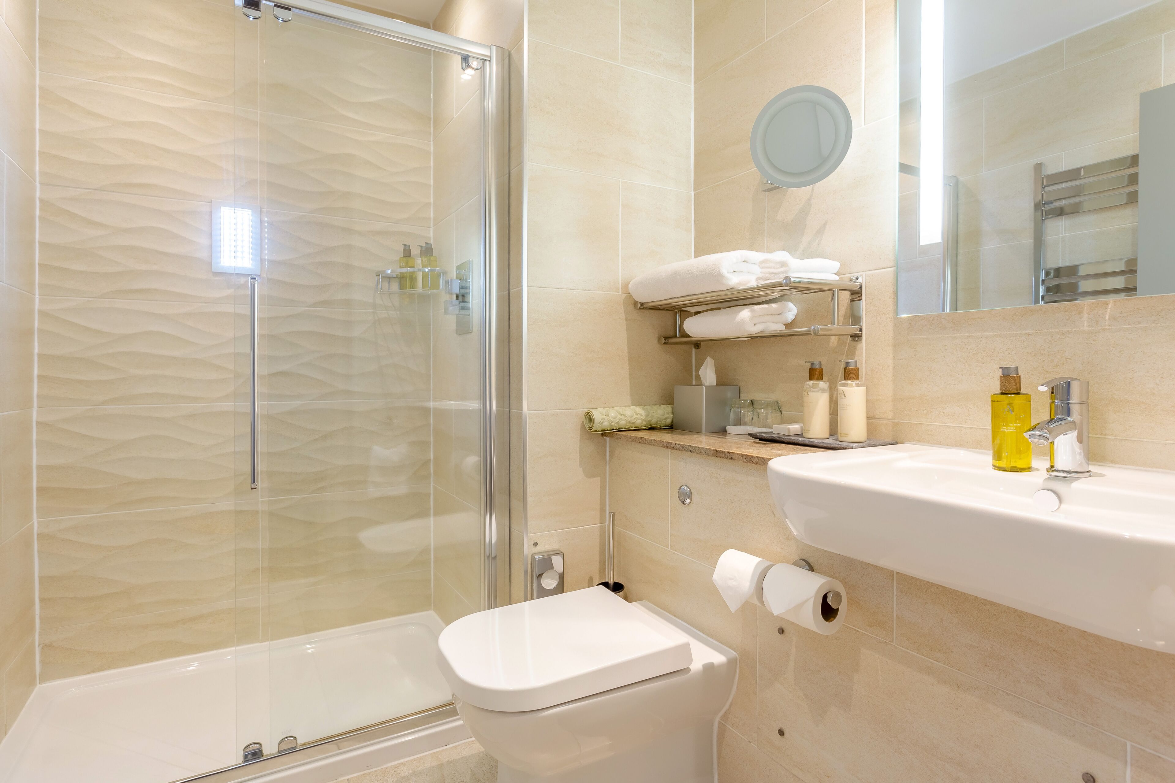 A modern bathroom with a glass shower enclosure, a white toilet, and a sink with toiletries.