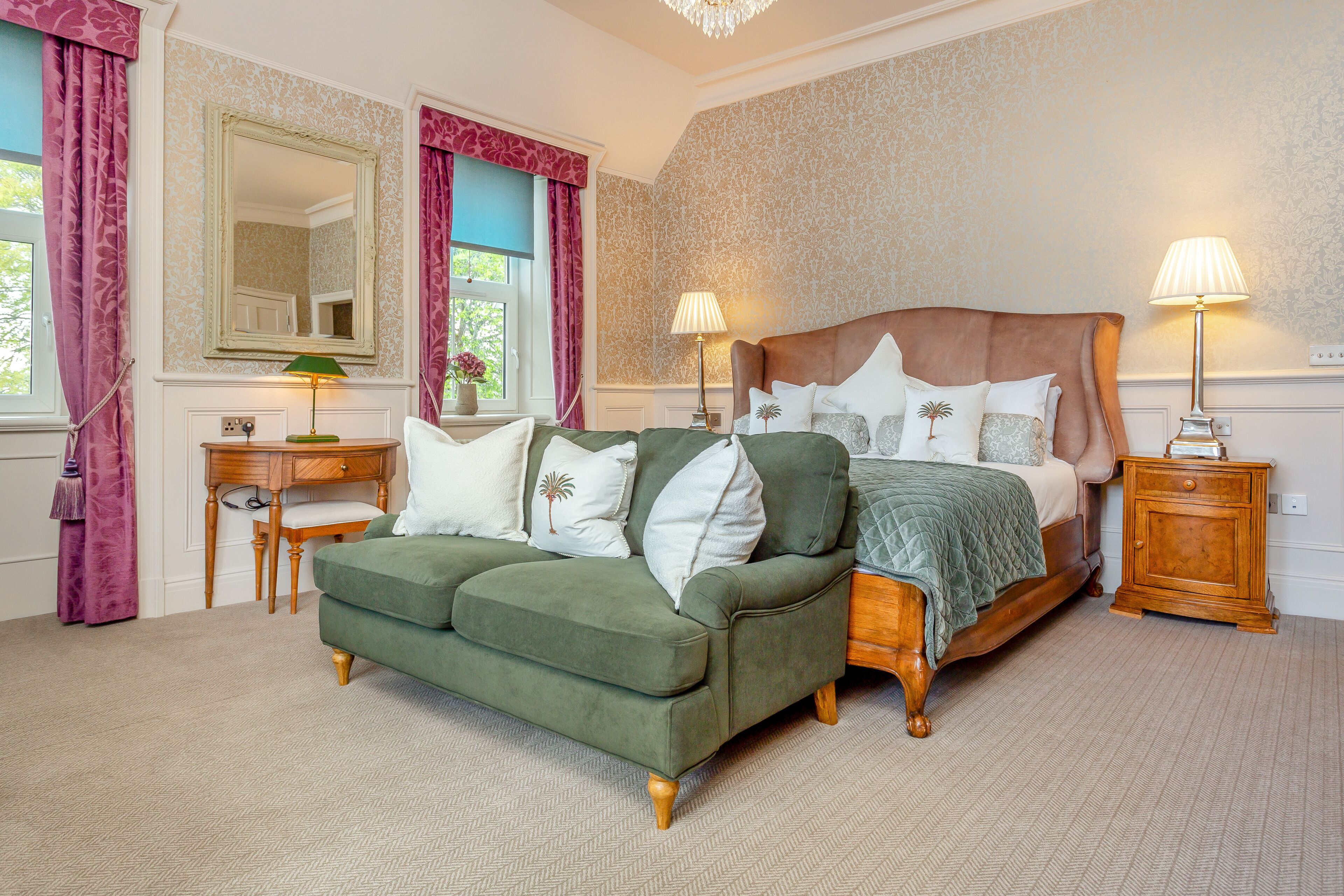 A bedroom with a bed, a green sofa, a wooden nightstand, a desk, and a mirror.