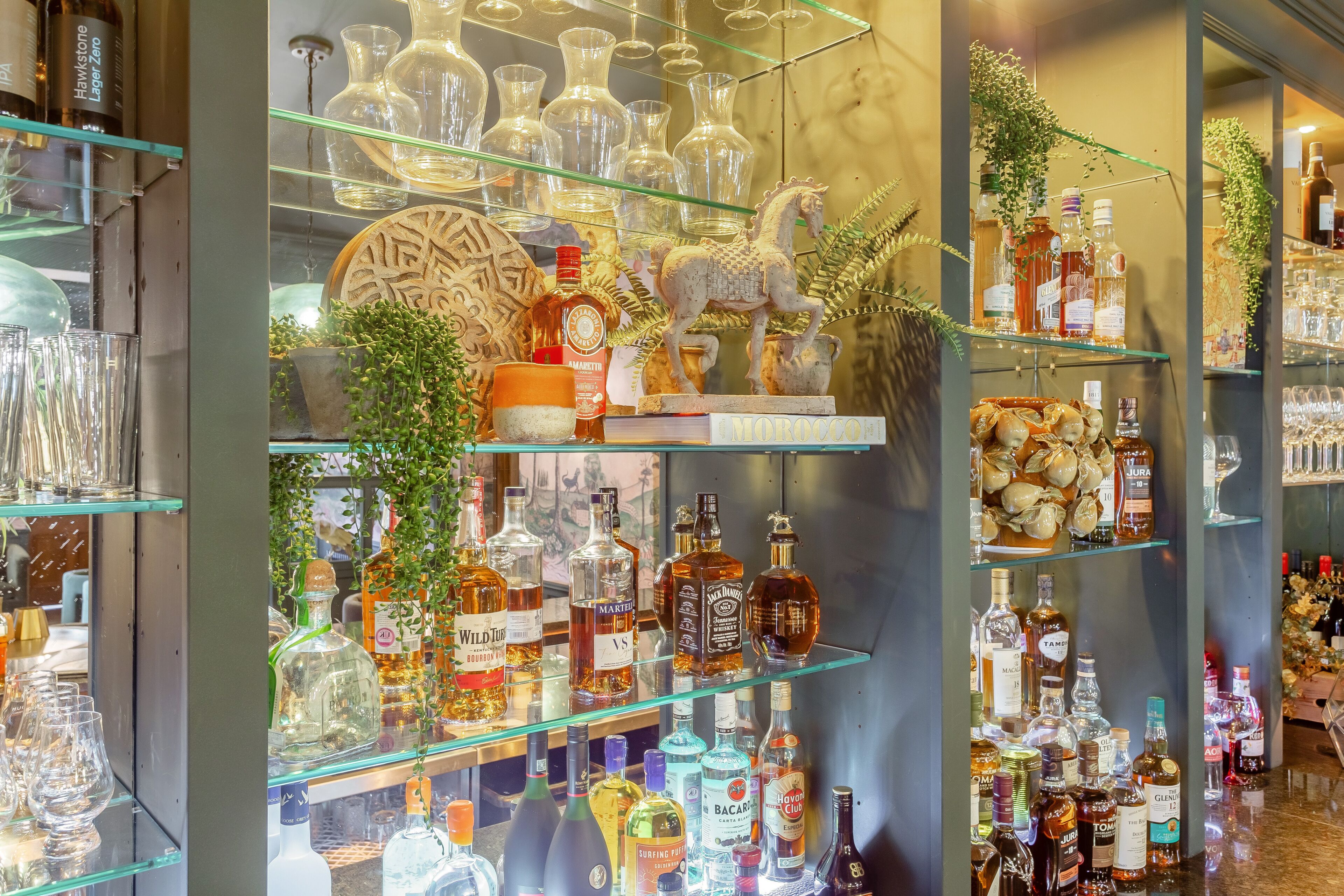 A bar area with shelves of liquor bottles, glasses, and decorative items.