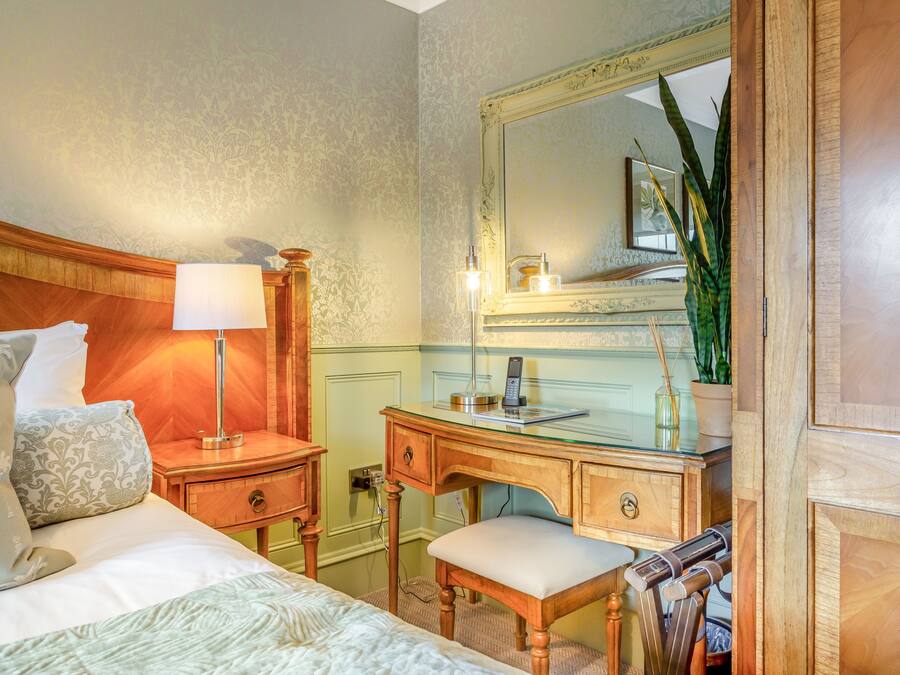 Et hotelværelse med en seng, et skrivebord, en stol, en lampe, et spejl og en potteplante.