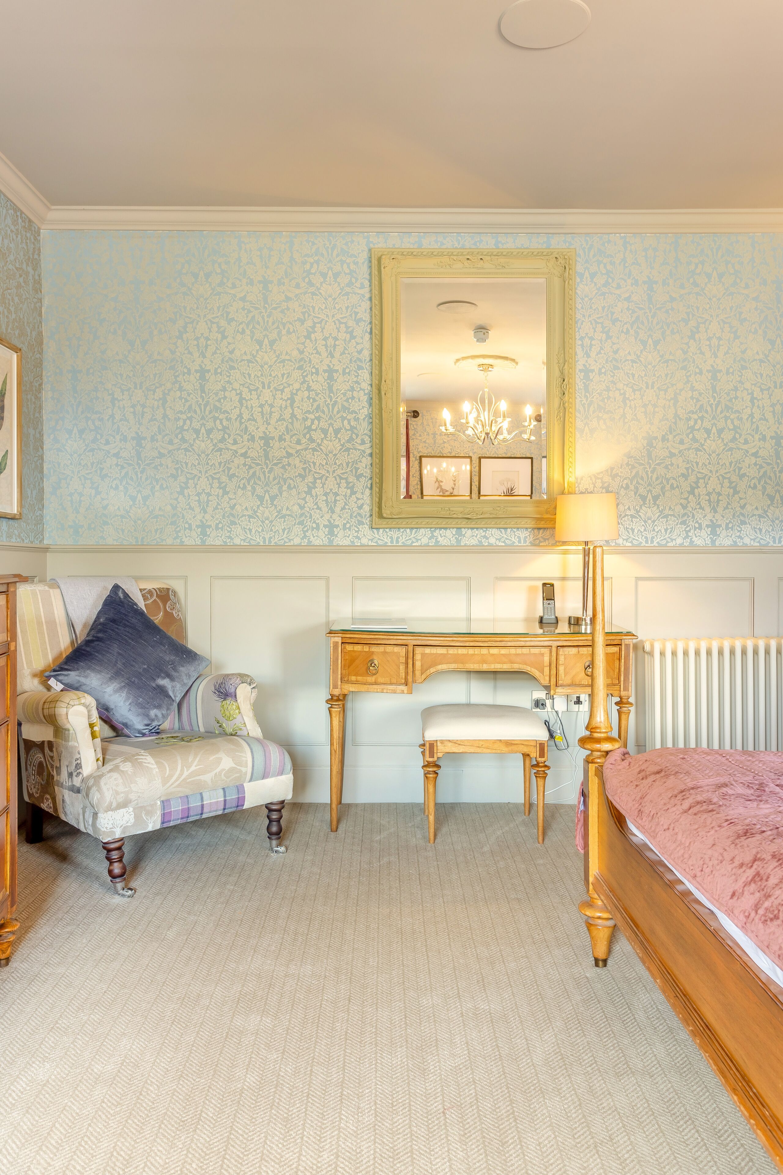 A bedroom with a bed, a chair, a desk, a mirror, and a radiator.