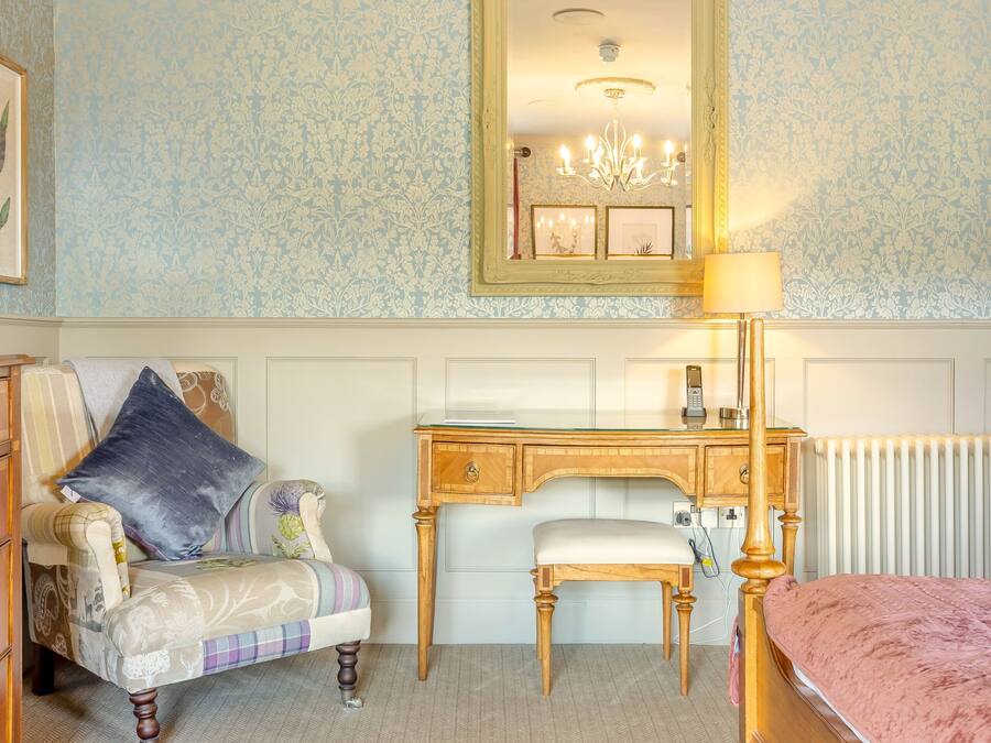 A bedroom with a bed, a chair, a desk, a mirror, and a radiator.