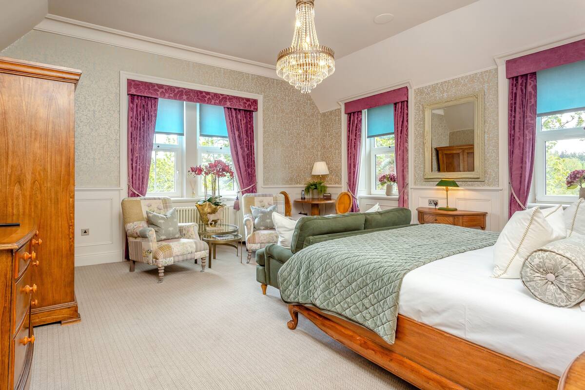 Un dormitorio con cama, dos sillas, cómoda, espejo y candelabro.
