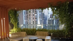 Un'area salotto esterna moderna con panchina, tavoli e fioriere, con vista sulla città.
