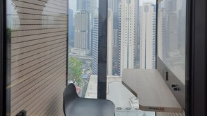 Una camera moderna con una grande finestra che offre vista sullo skyline cittadino, comprensivo delle Petronas Towers. Nella stanza si trova una piccola sedia nera e un tavolo bianco.