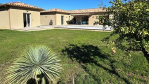 Une maison à deux étages, avec un toit en tuiles, une terrasse couverte et une pelouse bien entretenue.