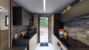 Uma cozinha moderna com armários escuros, bancada preta e vista para um pátio externo.