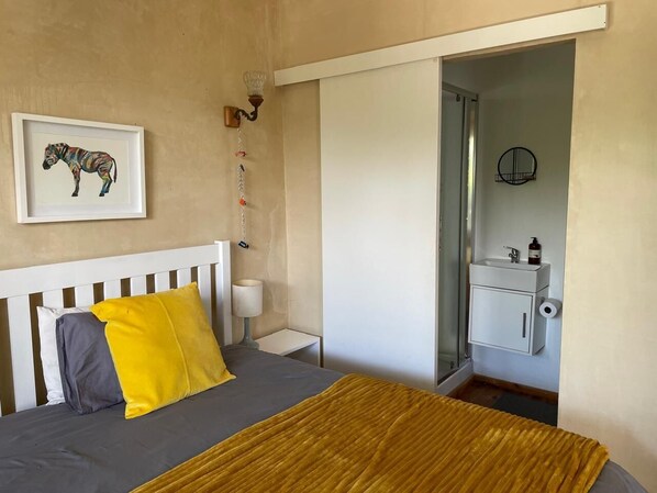 A bedroom with a bed, a bedside table, a lamp, a framed zebra artwork, and a bathroom with a sink and toilet.