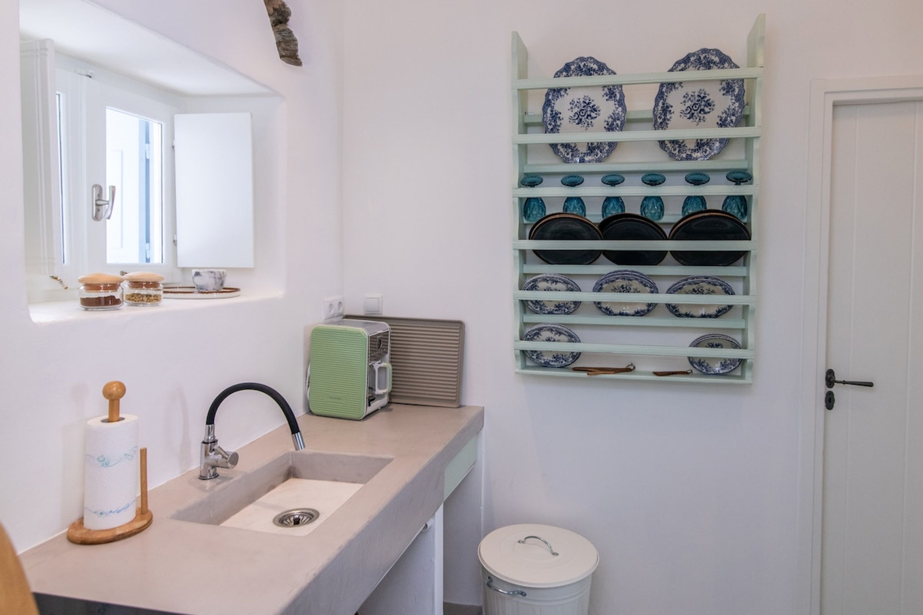 A bathroom with a sink, mirror, and a wall-mounted dish rack with plates.