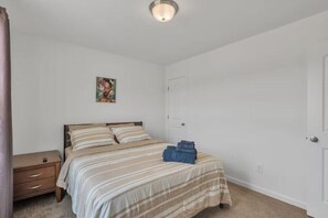 Un dormitorio con cama, mesita de noche, una puerta y una lámpara de pared.