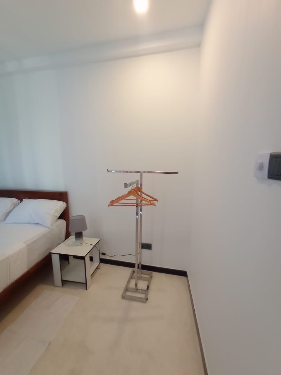 Ein Hotelzimmer mit einem Bett, einem Nachttisch mit Lampe, einem kleinen Tisch und einem Kleiderständer.