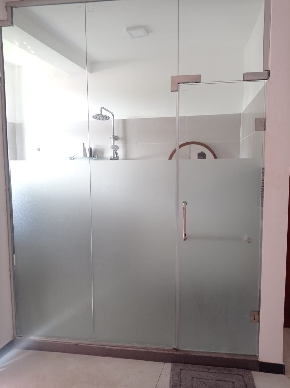 Casa de banho moderna com cabine de chuveiro em vidro, chuveiro manual e sanita visível.
