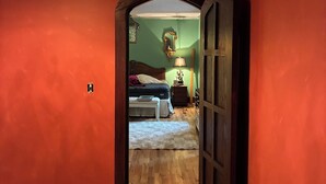 Un pasillo con piso a cuadros que conduce a un dormitorio con cama, mesita de noche, lámpara y un espejo en la pared.