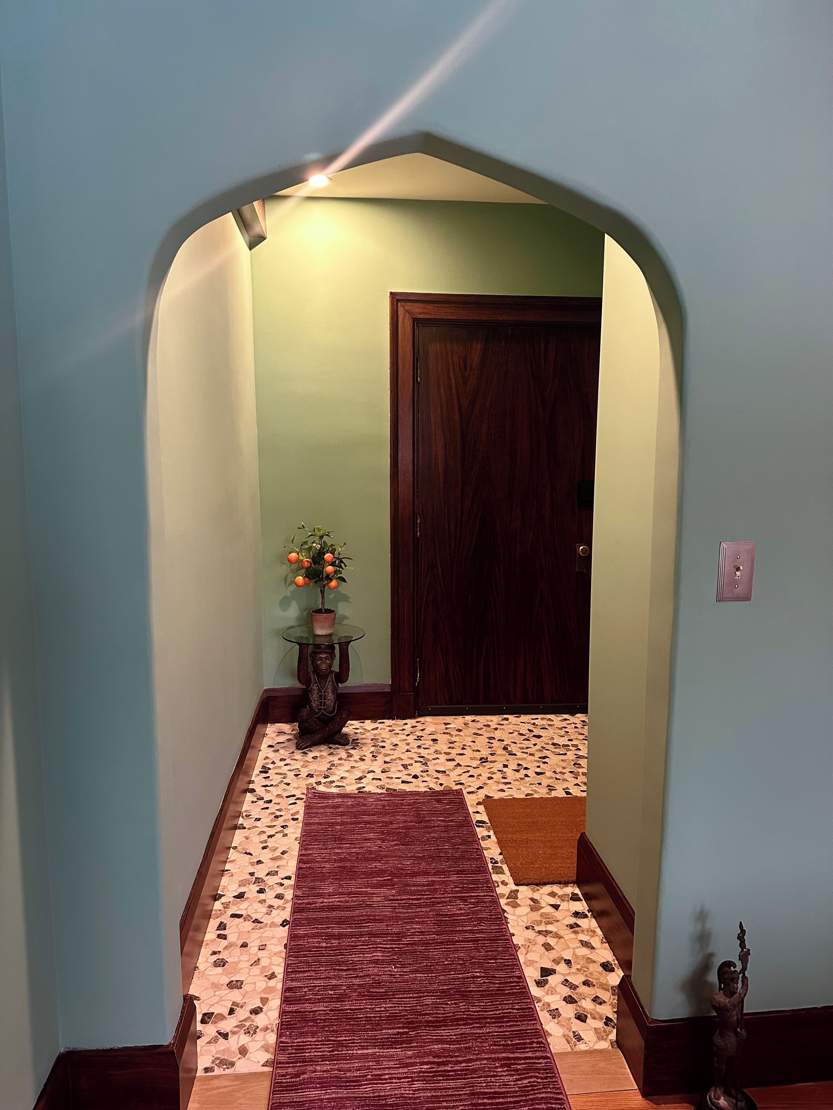 A hallway with a patterned floor, a red rug, a statue, and a door.