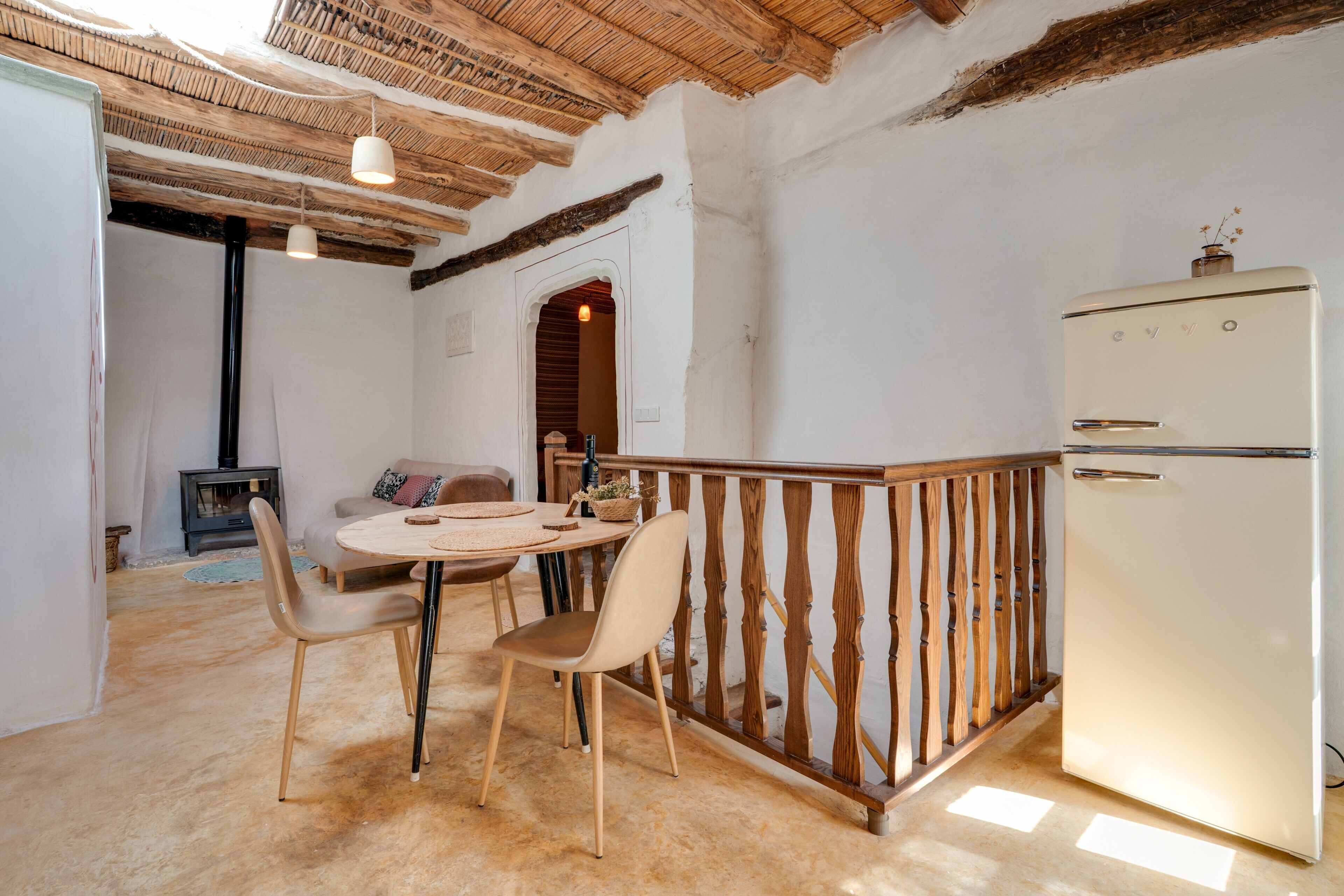 Una cocina rústica con techo de madera, un refrigerador blanco y una zona de comedor con dos sillas y una mesa redonda.