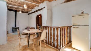 Una cocina rústica con techo de madera, un refrigerador blanco y una zona de comedor con dos sillas y una mesa redonda.
