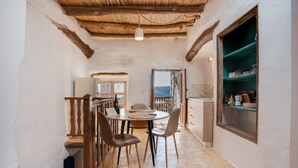 Un pasillo estrecho con techo de madera, un comedor con una mesa redonda y sillas, y una cocina con un estante verde.