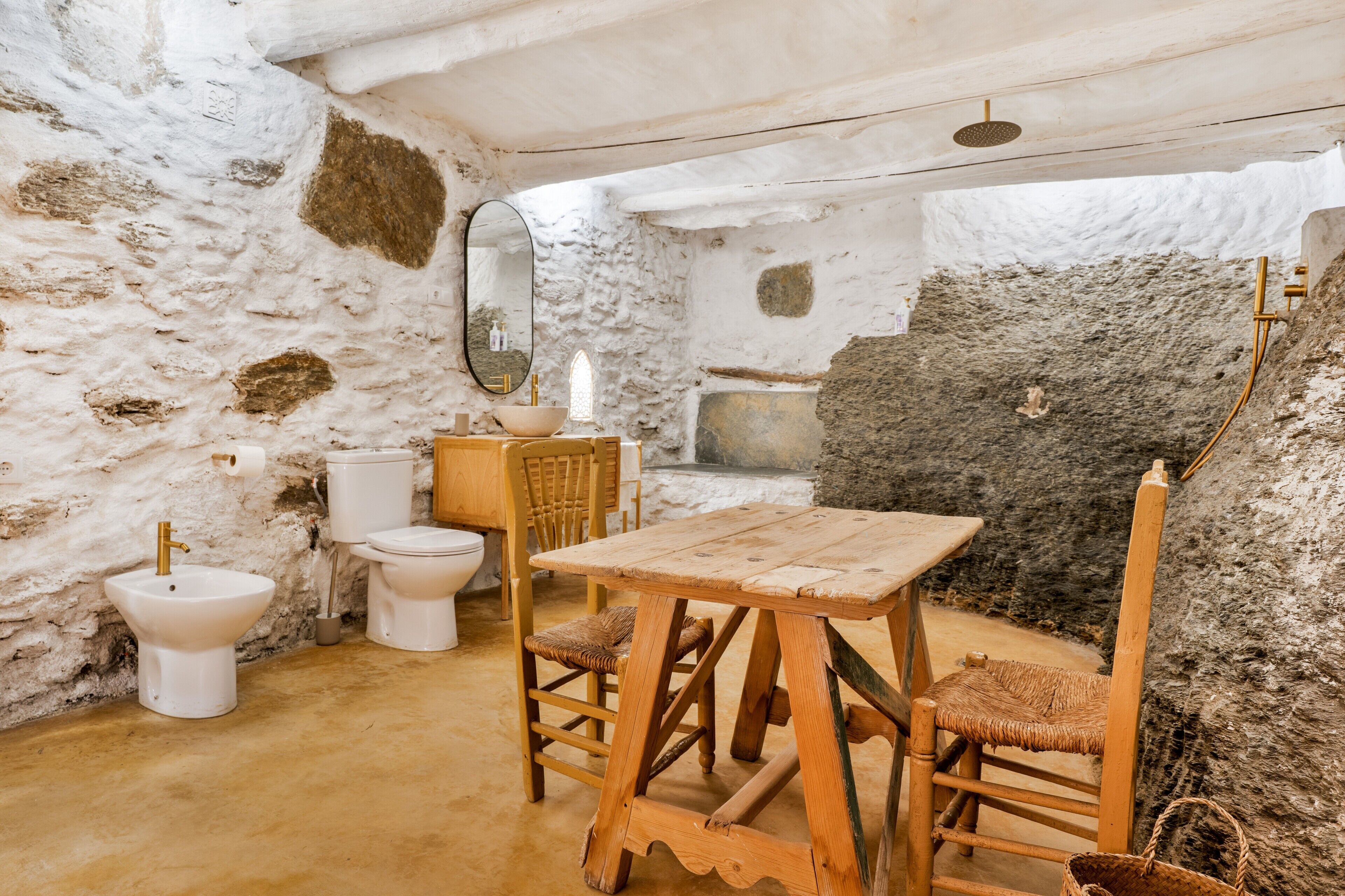 A rustic bathroom with a stone wall, a wooden table, and a wooden chair.
