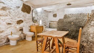 A rustic bathroom with a stone wall, a wooden table, and a wooden chair.