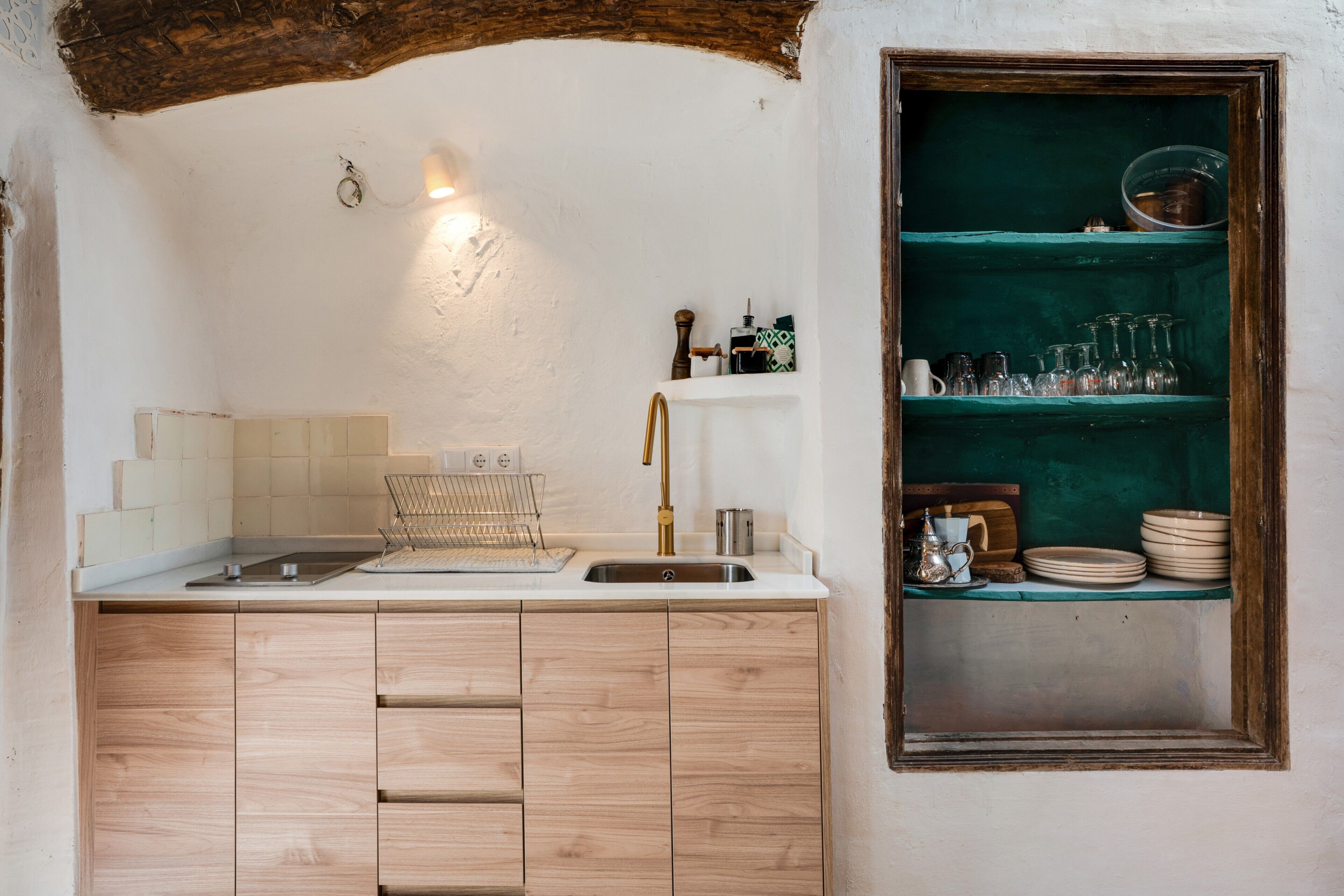A kitchen with a wooden cabinet, a sink, and a shelf with glassware and plates.