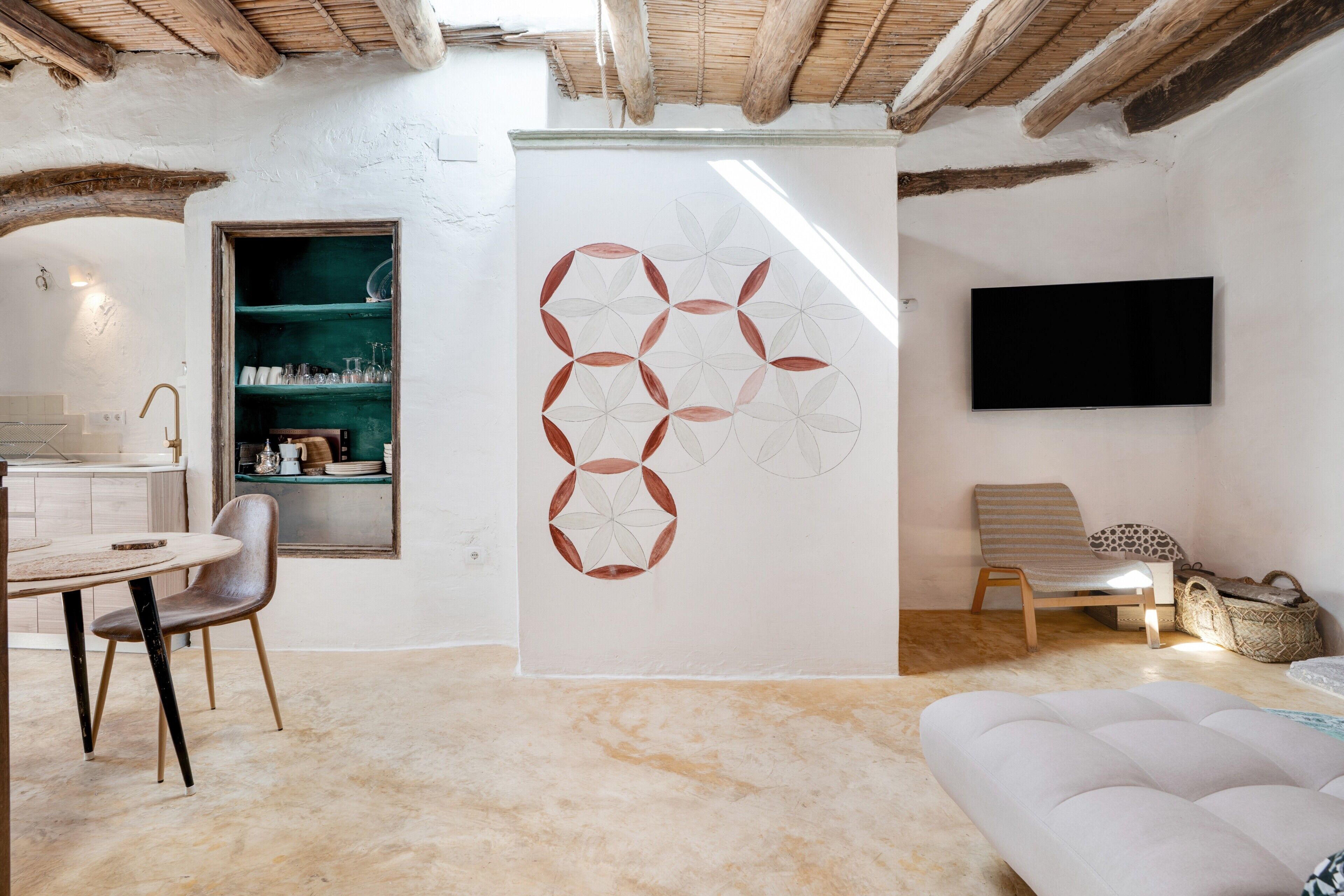 A room with a dining area, a sofa, a TV mounted on the wall, and a geometric wall art piece.