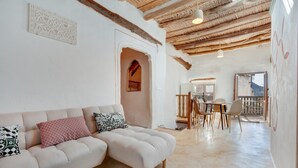 Una sala de estar con sofá, un comedor con sillas, techo de madera y vista a través de un ventanal.