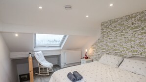 A bedroom with a skylight, a bed with a rolled towel, a chair, and a nightstand with a candle. - 1 Castle Terrace (Thirsk)