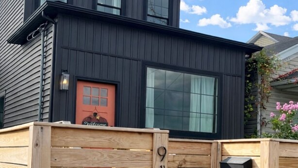 Ett modernt hus i två våningar med en mörk fasad, stora fönster och ett trästaket med en brevlåda.