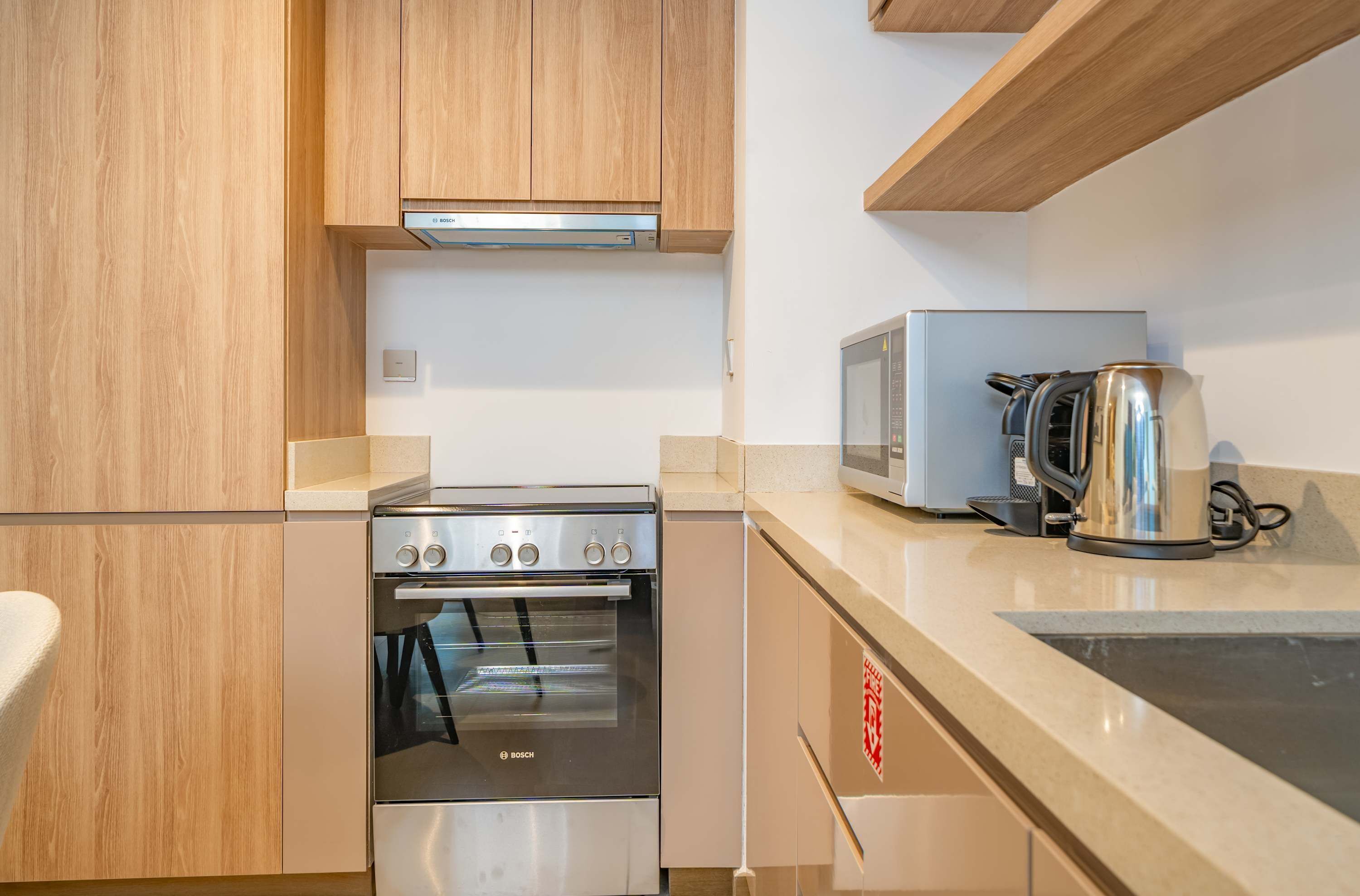 Una cocina con armarios de madera, horno Bosch, microondas y hervidor.