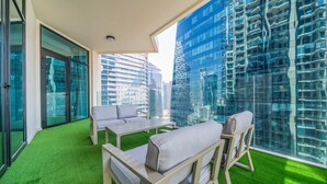 Un interior moderno con piso de césped artificial verde, un sofá, una mesa de centro y un muro de vidrio que ofrece vistas de edificios altos.
