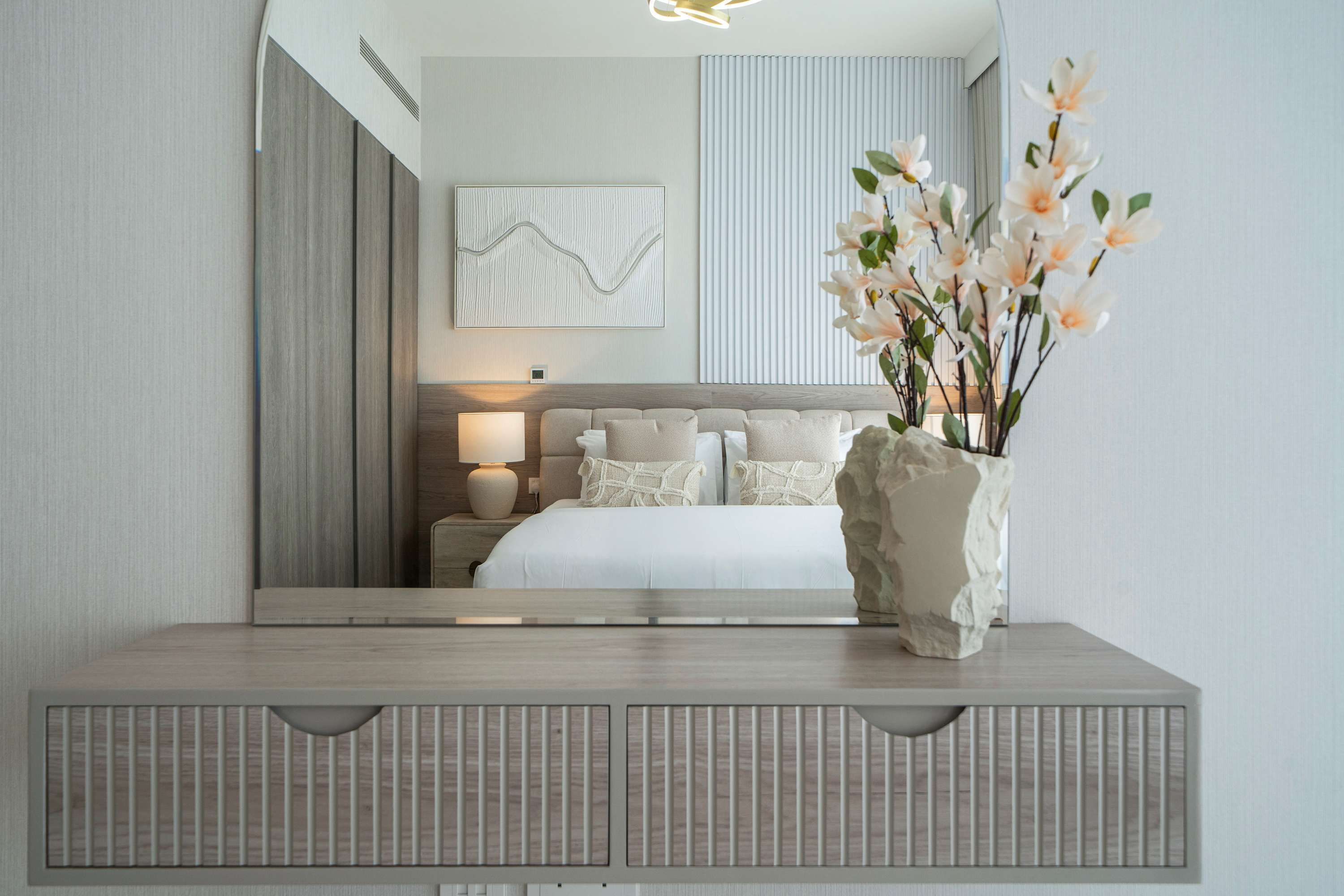Ein modernes Schlafzimmer mit einem großen Bett, einem Nachttisch, einem Wandbild und einer Vase mit Blumen.