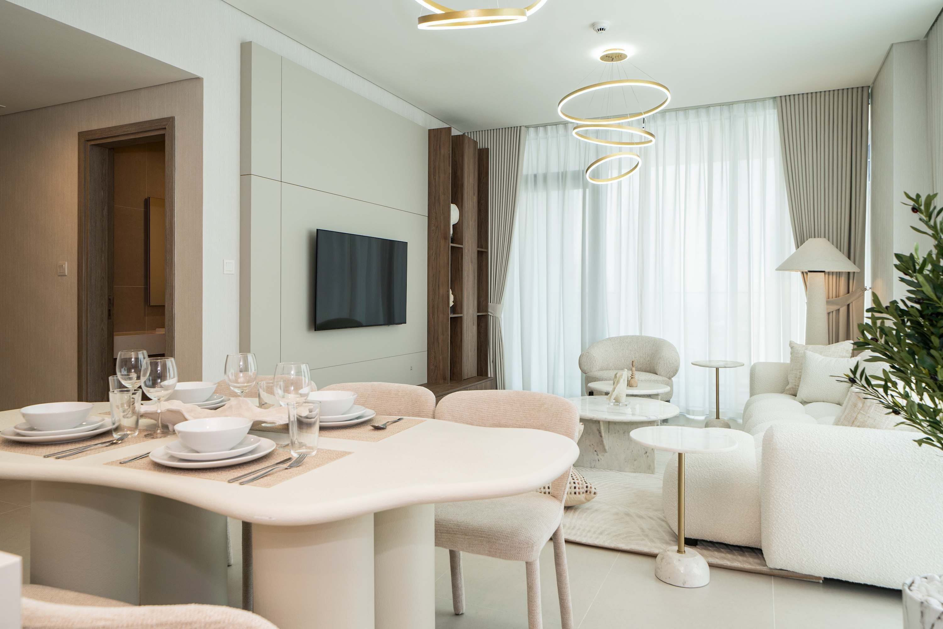 Een moderne woonkamer met een eethoek, een zithoek en een aan de muur bevestigde televisie.