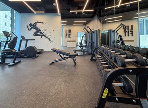 Une salle de sport équipée de matériel d’exercice, ornée d’une fresque murale et dotée de grandes fenêtres.