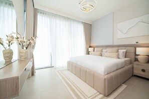 Ein modernes Schlafzimmer mit einem großen Bett, Nachttischen, einem Spiegel und Blick ins Freie.