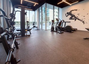 Ein Fitnessstudio mit verschiedenen Trainingsgeräten, großen Fenstern und Wandgemälden.