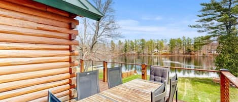 A wooden deck with a table and chairs, overlooking a lake and forest.