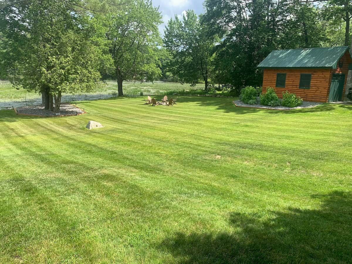 A well-maintained grassy lawn with a wooden cabin and a picnic table.