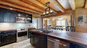 A rustic log home kitchen perfectly blends natural charm with modern luxury.  log walls and exposed wooden beams create an authentic, warm atmosphere, centered around a large, custom-built island with a thick, butcher-block countertop.  - Luxurious Lakefront Log Home with Private Dock (Augusta)