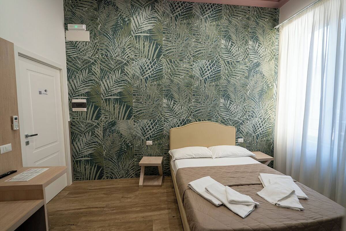 A hotel room with a bed, a nightstand, a desk, and a door.