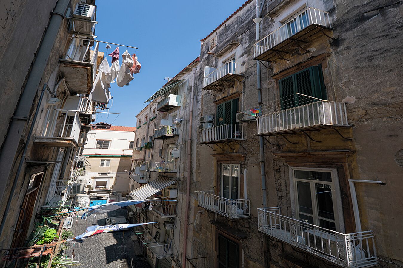 A narrow urban street with old buildings, balconies, and hanging laundry.