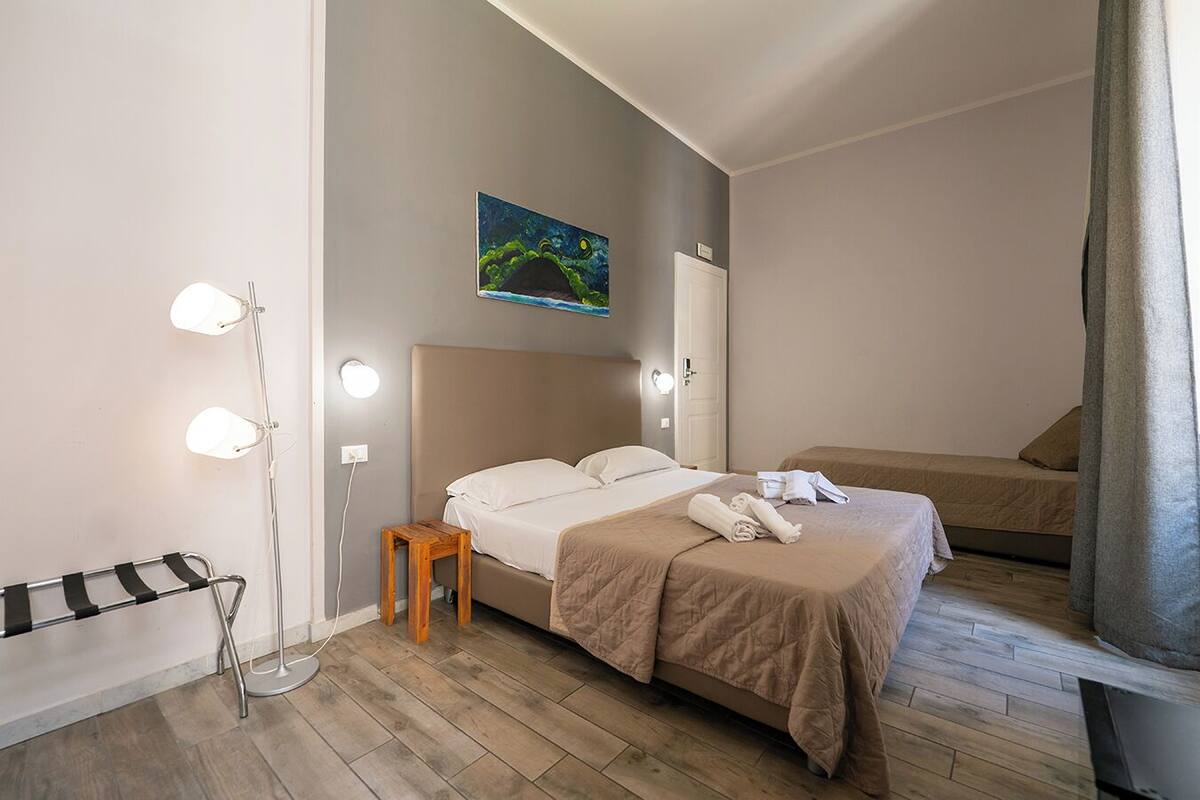 A hotel room with a bed, bedside table, lamp, and a painting on the wall.